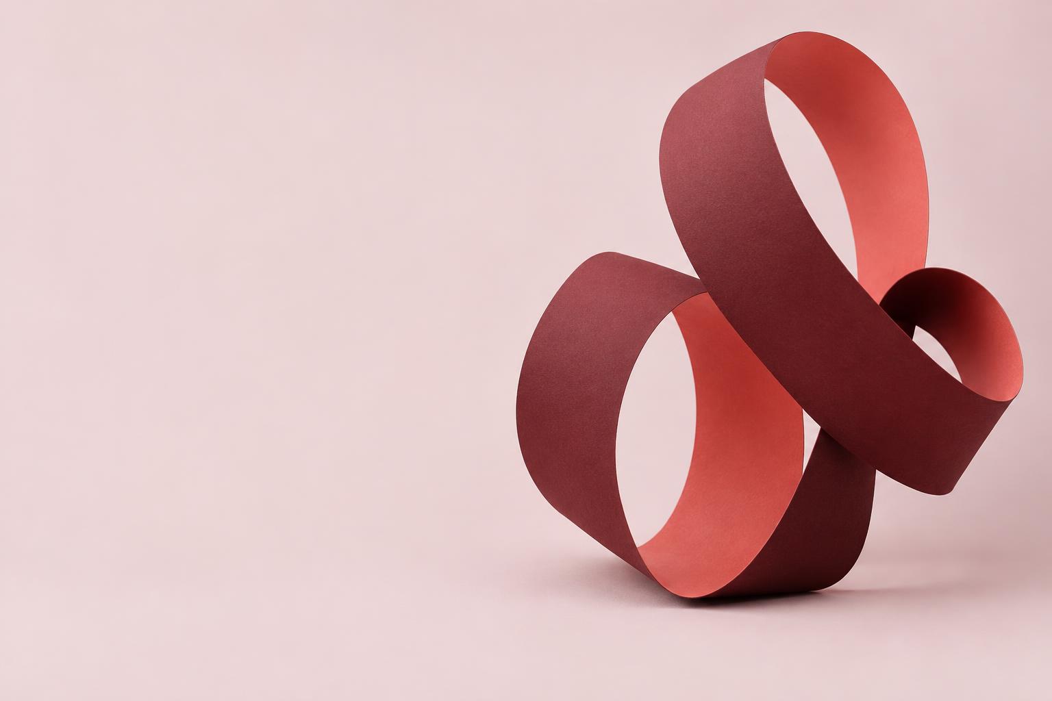 A sculptural burgundy paper ribbon forming an open, interconnected loop